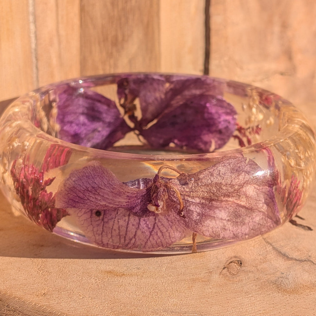 Handmade resin bangle with purple orchid petals and red wild flowers – close-up detail on wooden background – EL-Creations