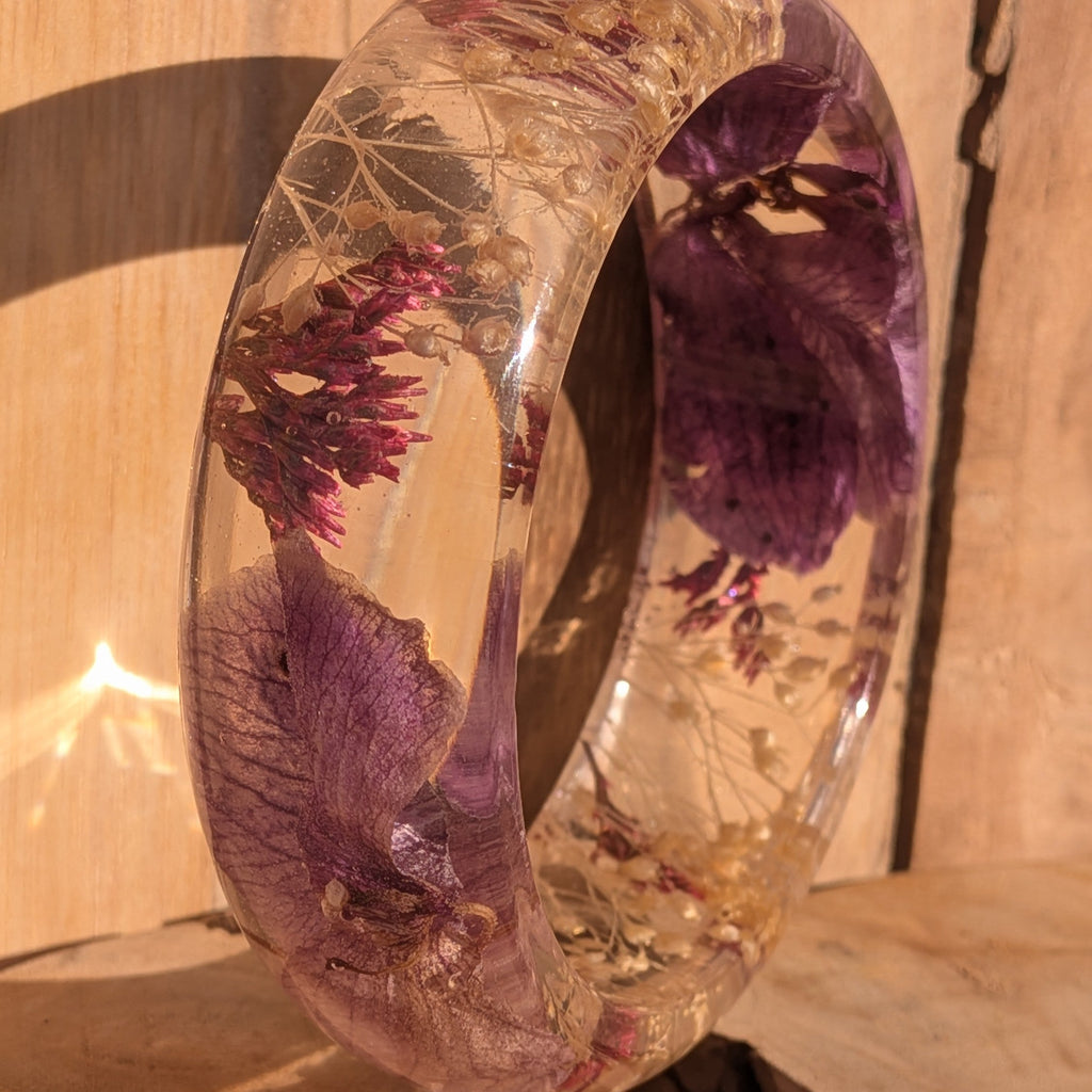Handmade resin bracelet with purple orchid petals and red wild flowers – wrist close-up in sunlight – EL-Creations