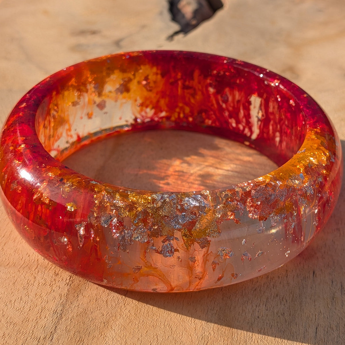 Side view of red orange epoxy resin bangle with gold silver leaf on wooden surface – EL-Creations