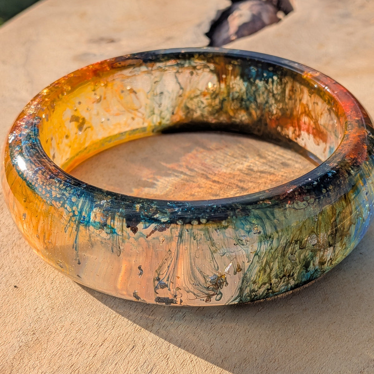Close-up of amber orange resin bangle surface with teal gold swirl detail – EL-Creations