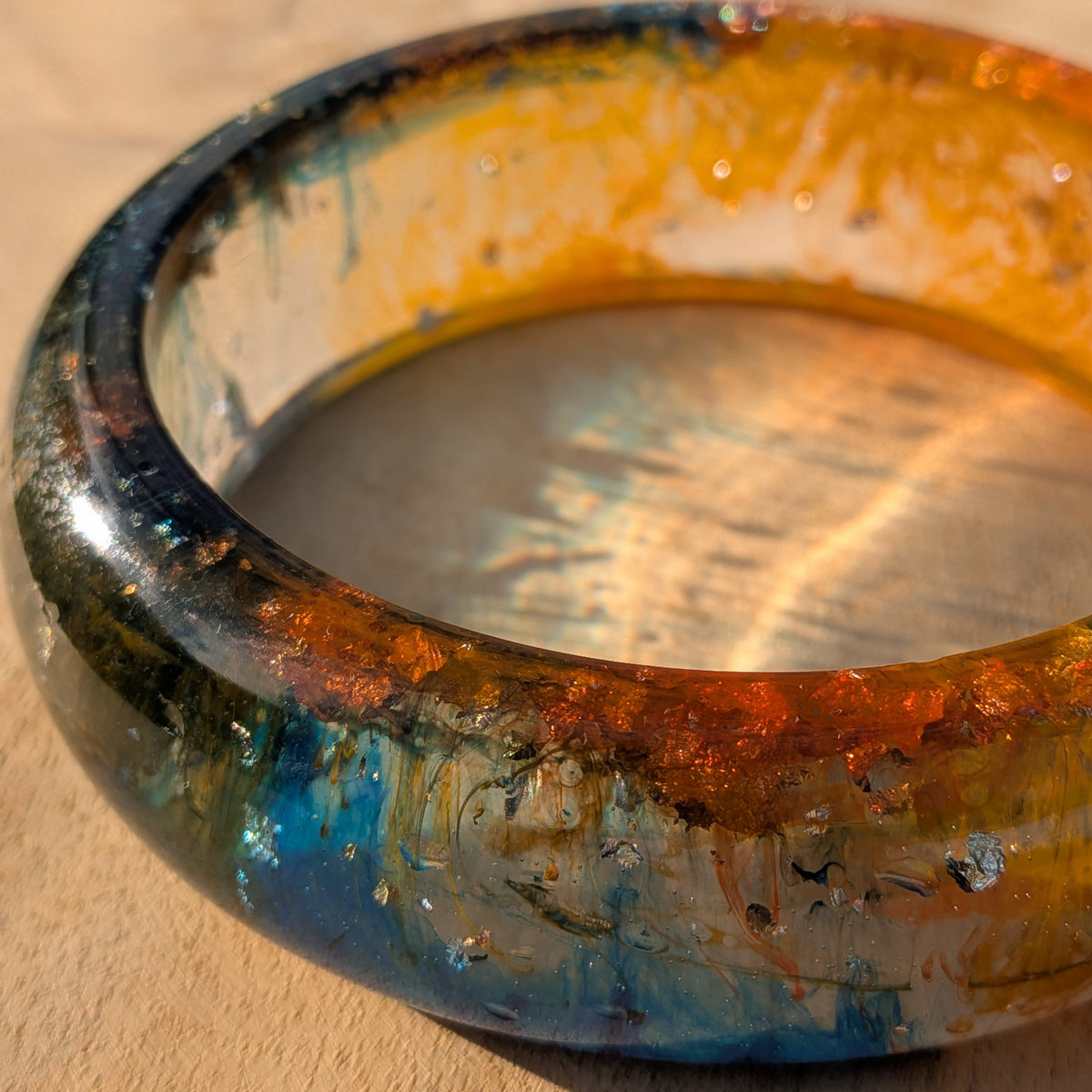 Macro detail of amber orange and teal epoxy resin bangle showing gold fleck texture – EL-Creations