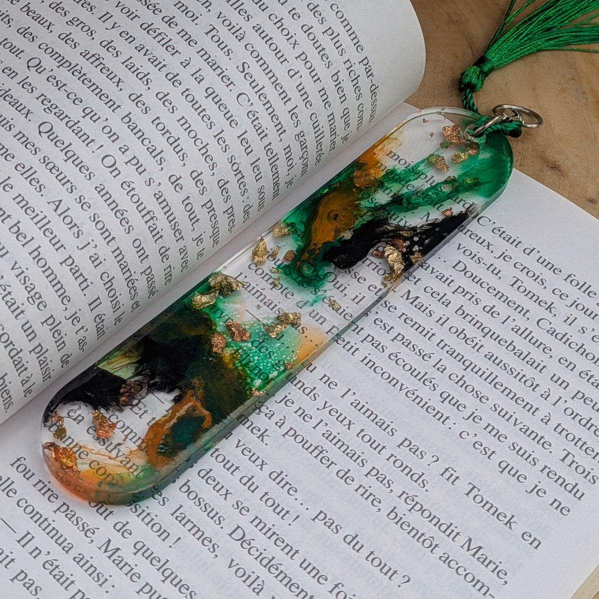 Green and gold resin bookmark keychain lying on open French book pages – EL-Creations