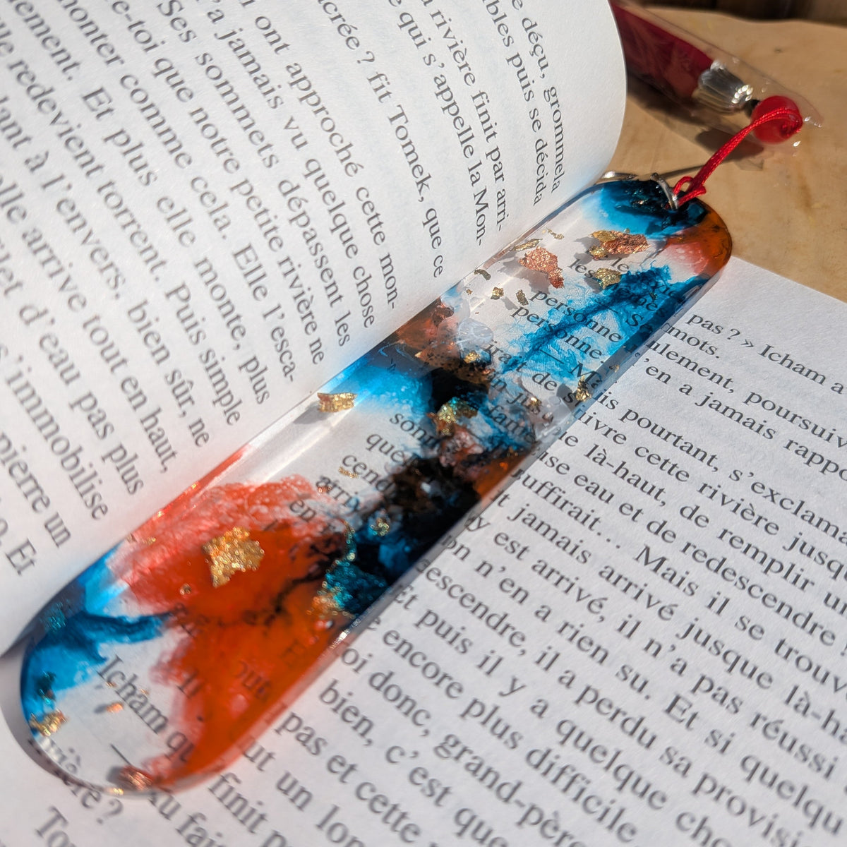 Handmade blue and orange resin bookmark with gold leaf lying in open French book spine – EL-Creations
