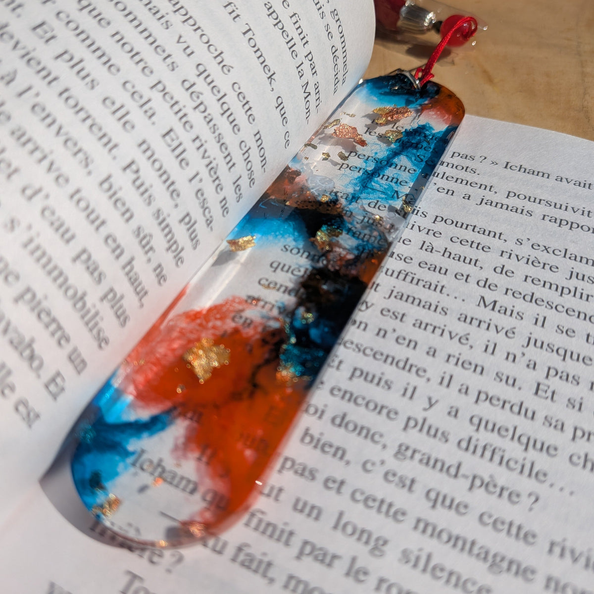 Burning tide resin bookmark with red tassel keychain on open book pages – EL-Creations