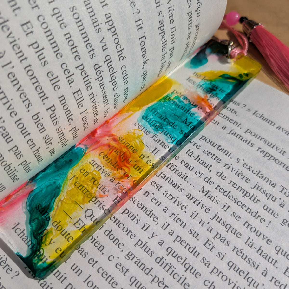 Handmade yellow teal and pink resin bookmark lying diagonally across open French book – EL-Creations