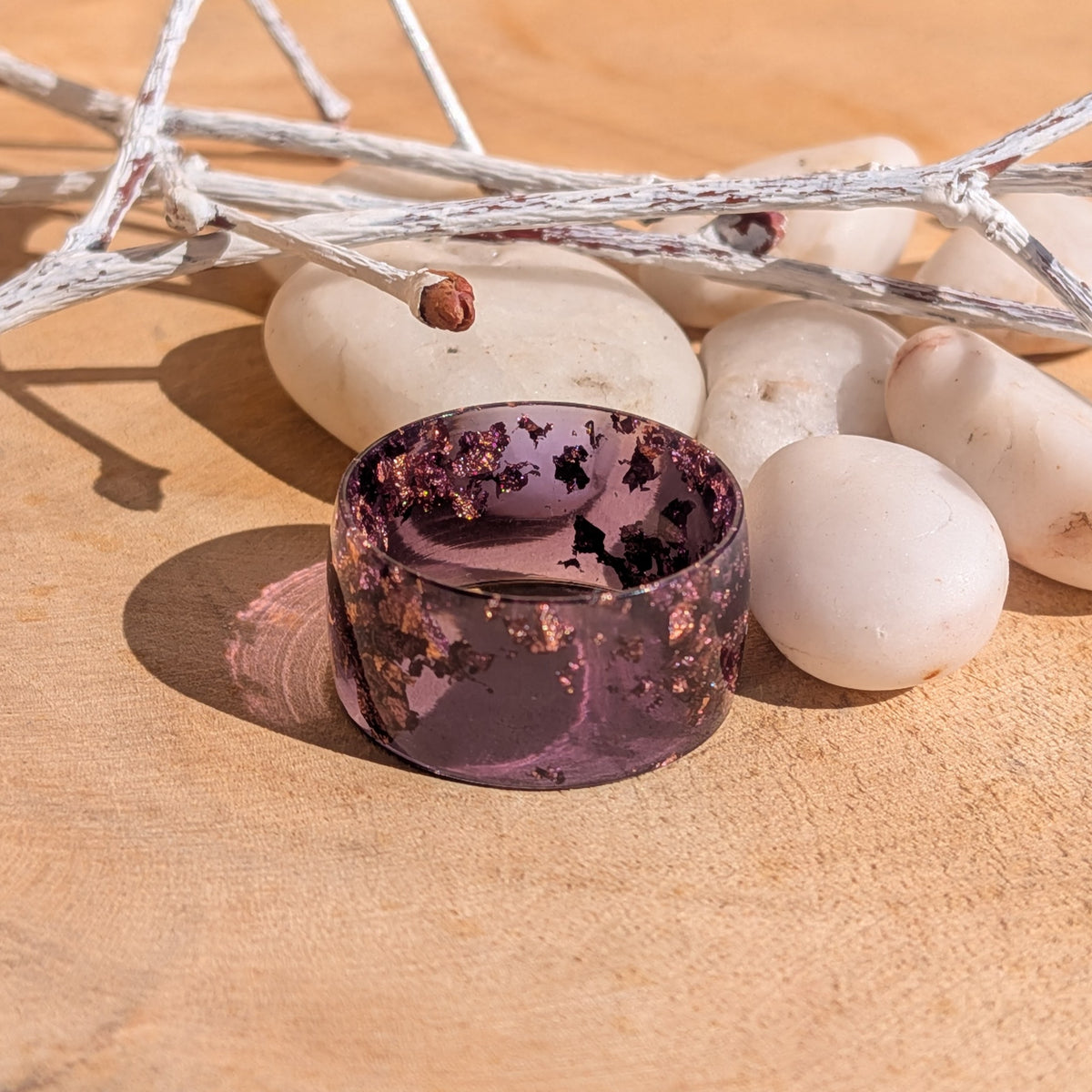 Purple resin wide-band ring with copper flakes beside white pebbles and silver-coloured branches, EL-Creations