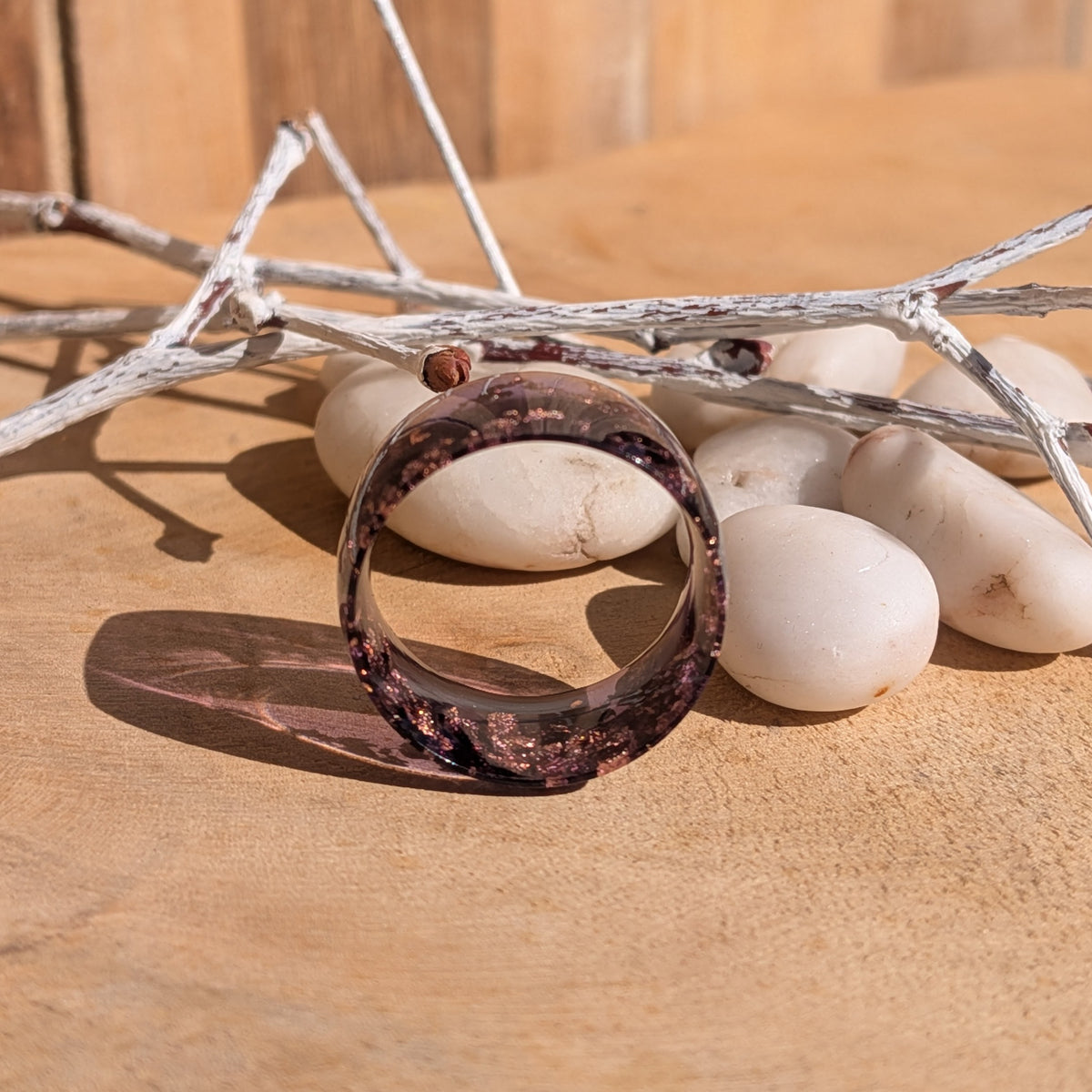 Purple copper flake resin ring standing upright, showing its circular opening beside white pebbles, EL-Creations