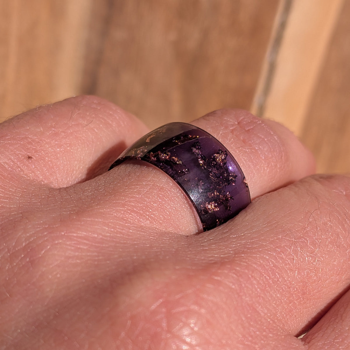 Angled close-up of a glossy purple resin ring with copper flakes worn on a finger, EL-Creations