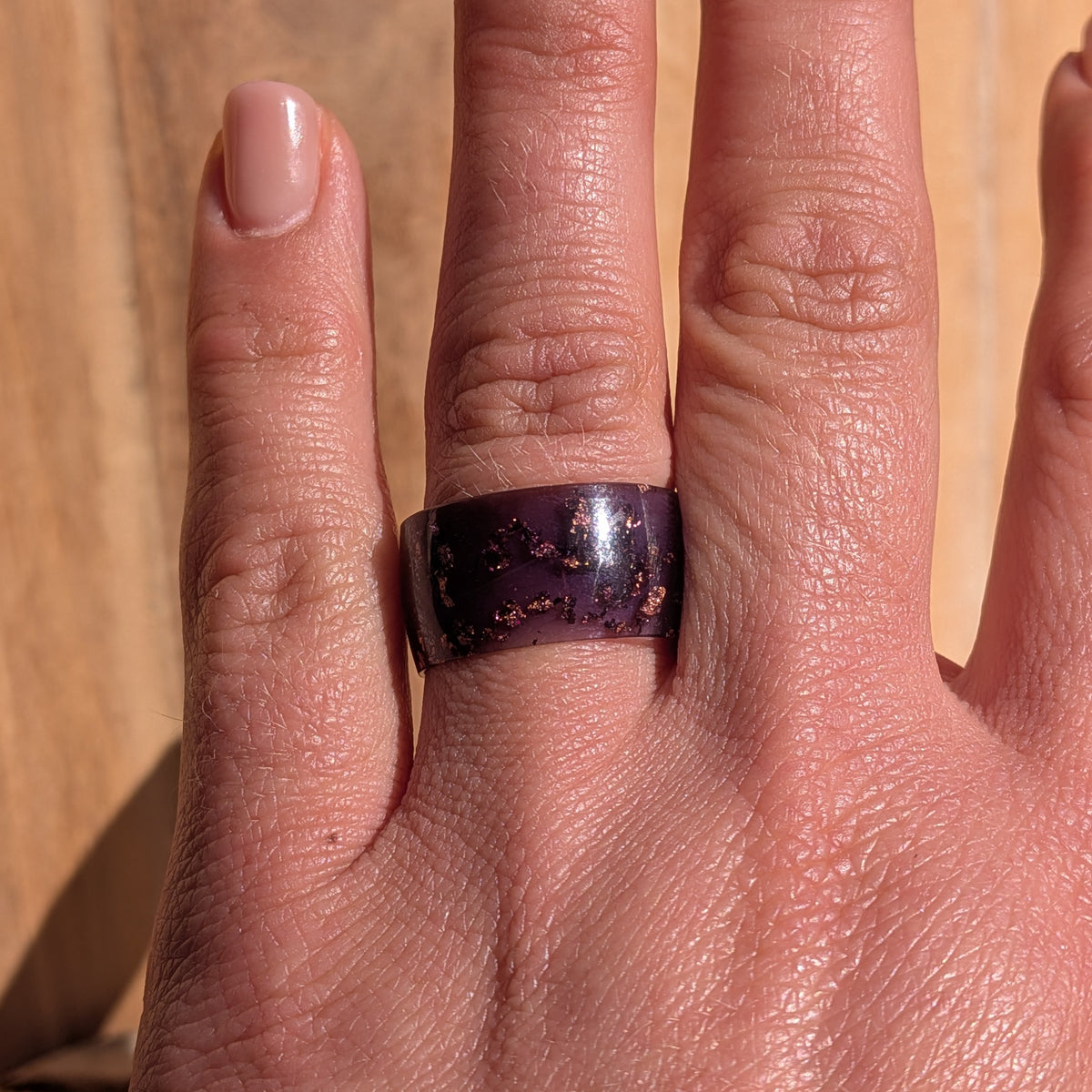 Front view of a wide purple resin ring with copper flakes worn on a hand in sunlight, EL-Creations