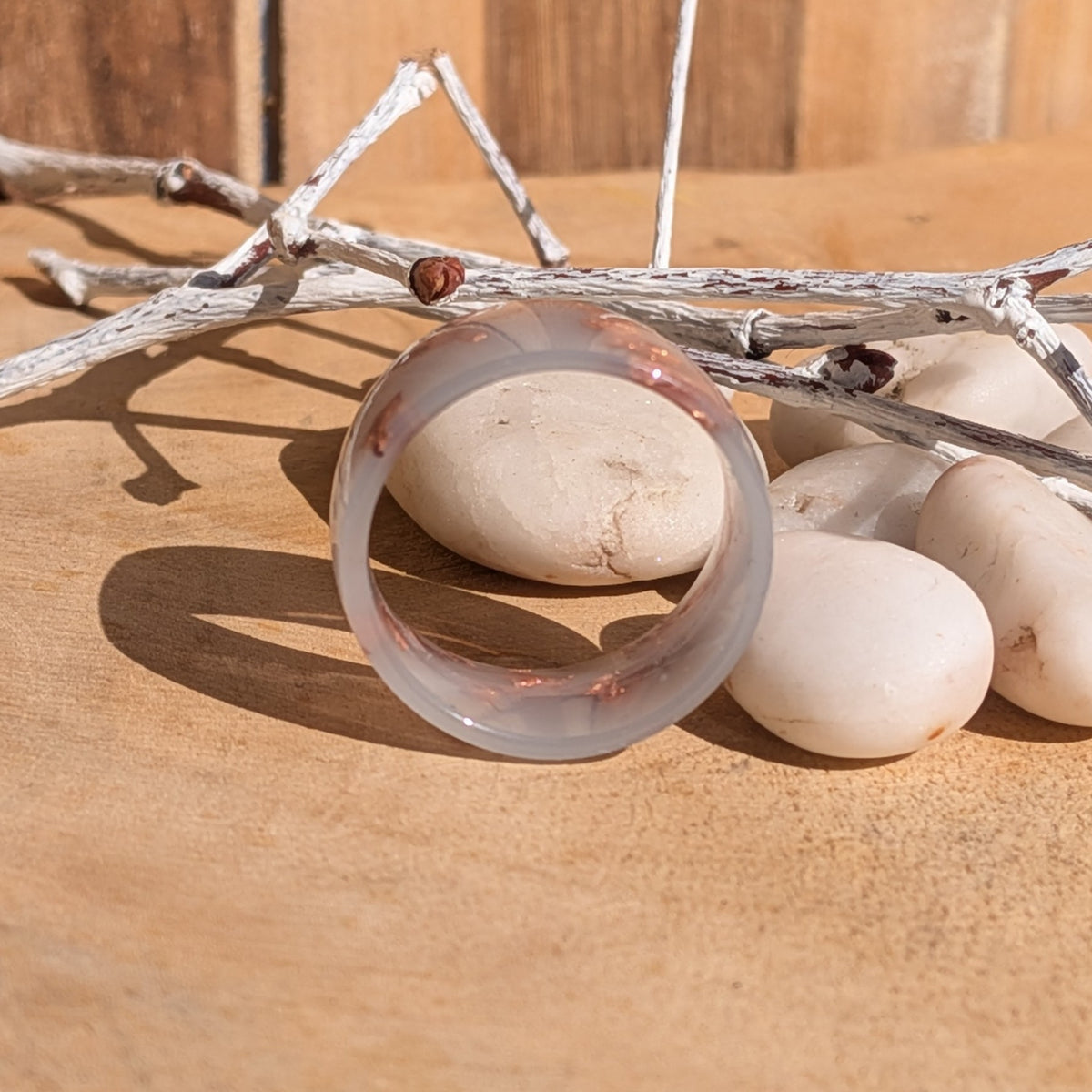 Milky lilac resin ring standing upright with its circular opening facing forward, beside white pebbles and decorative branches, EL-Creations