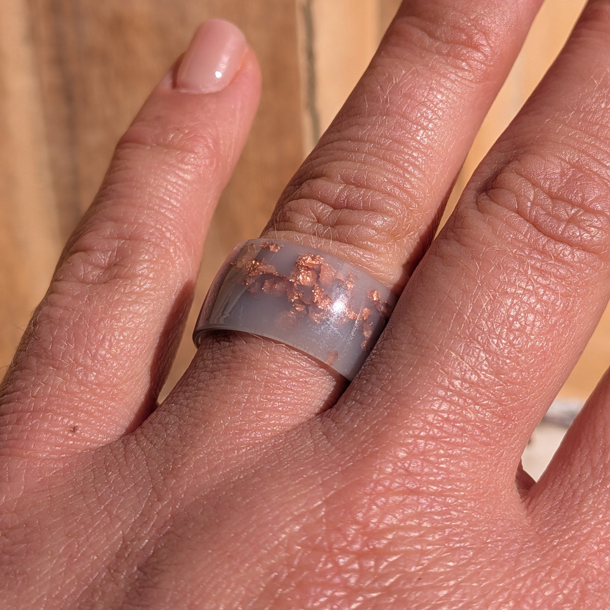 Close-up of a glossy milky lilac resin ring with copper flakes worn on a finger in sunlight, EL-Creations
