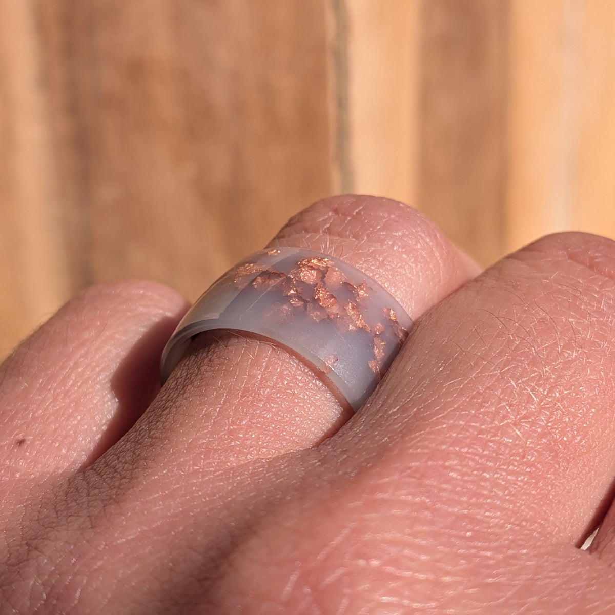Low angled close-up of a milky lilac resin wide-band ring worn on a finger, showing copper flakes beneath the glossy surface, EL-Creations