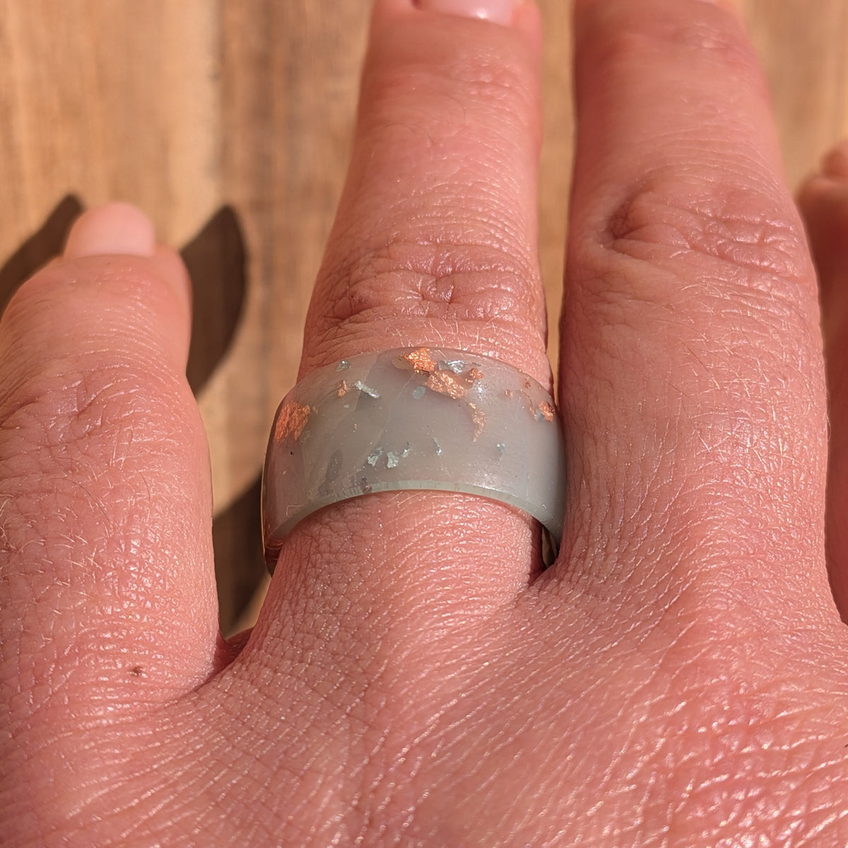 Front view of a milky blue-green resin ring with silver and copper flakes worn on a finger, showing the wide band, EL-Creations