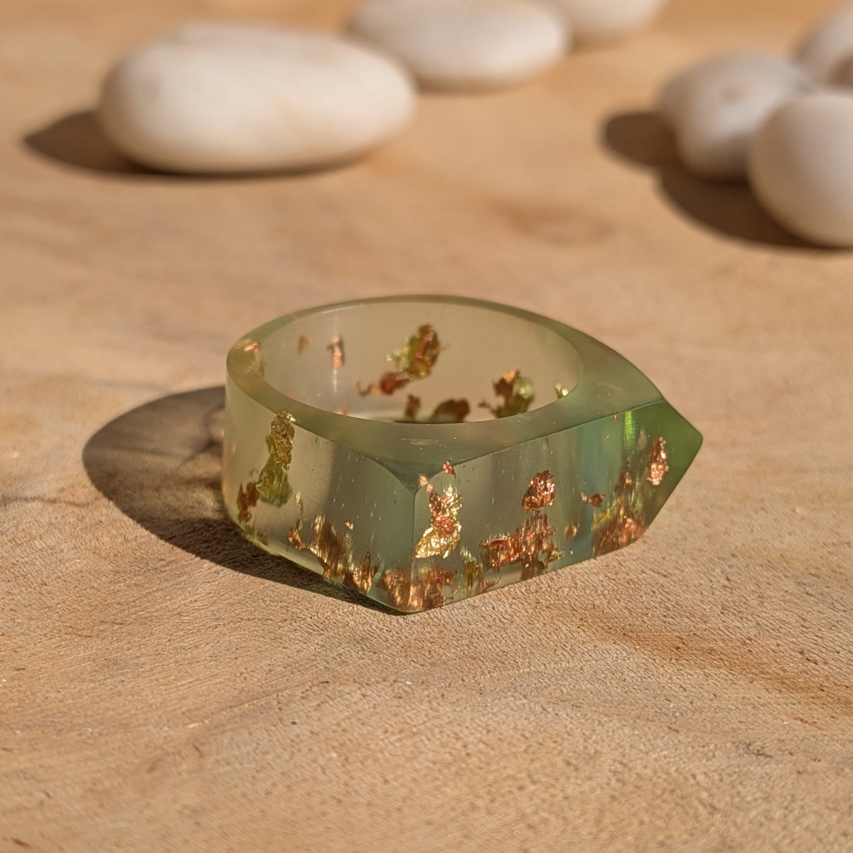 Angled view of a geometric green resin ring resting flat on wood, showing its faceted outer shape and metallic flakes, EL-Creations