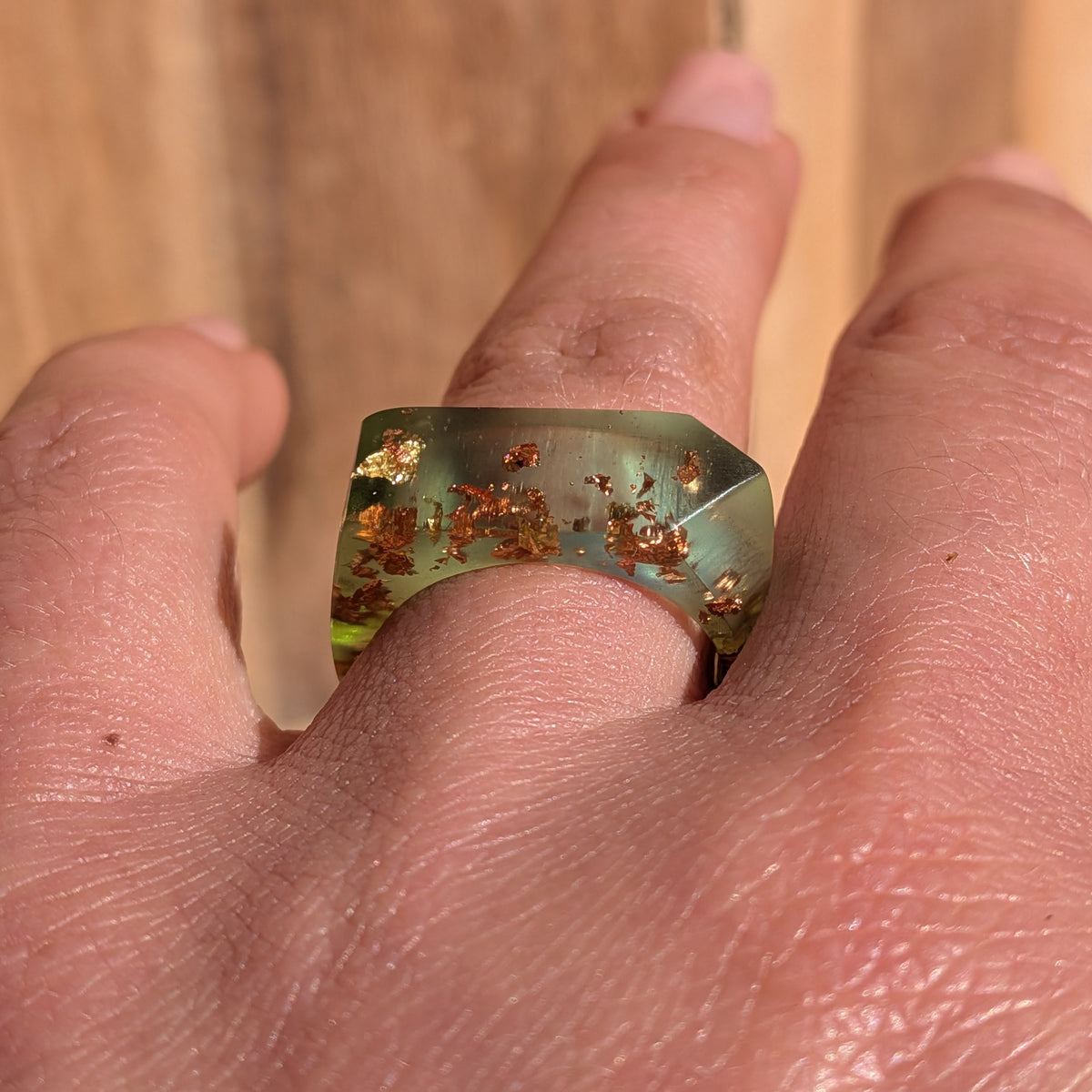 Front view of a geometric green resin statement ring with copper and gold flakes worn on a finger, EL-Creations