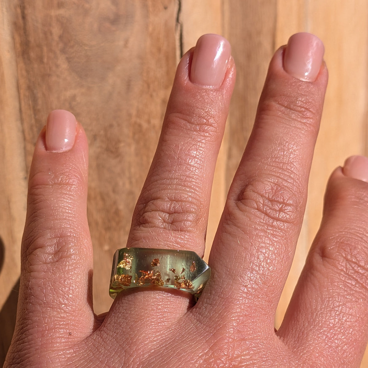 One-of-a-kind geometric green resin ring with copper and gold flakes worn on an outstretched hand against a wooden background, EL-Creations