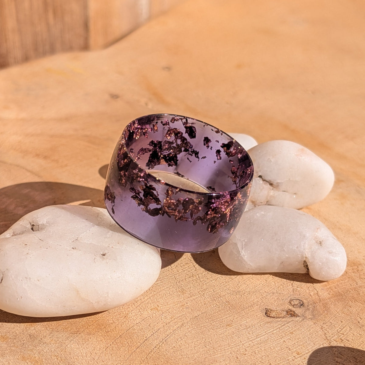 Wide purple resin ring with copper flakes and a glossy finish beside white pebbles, EL-Creations