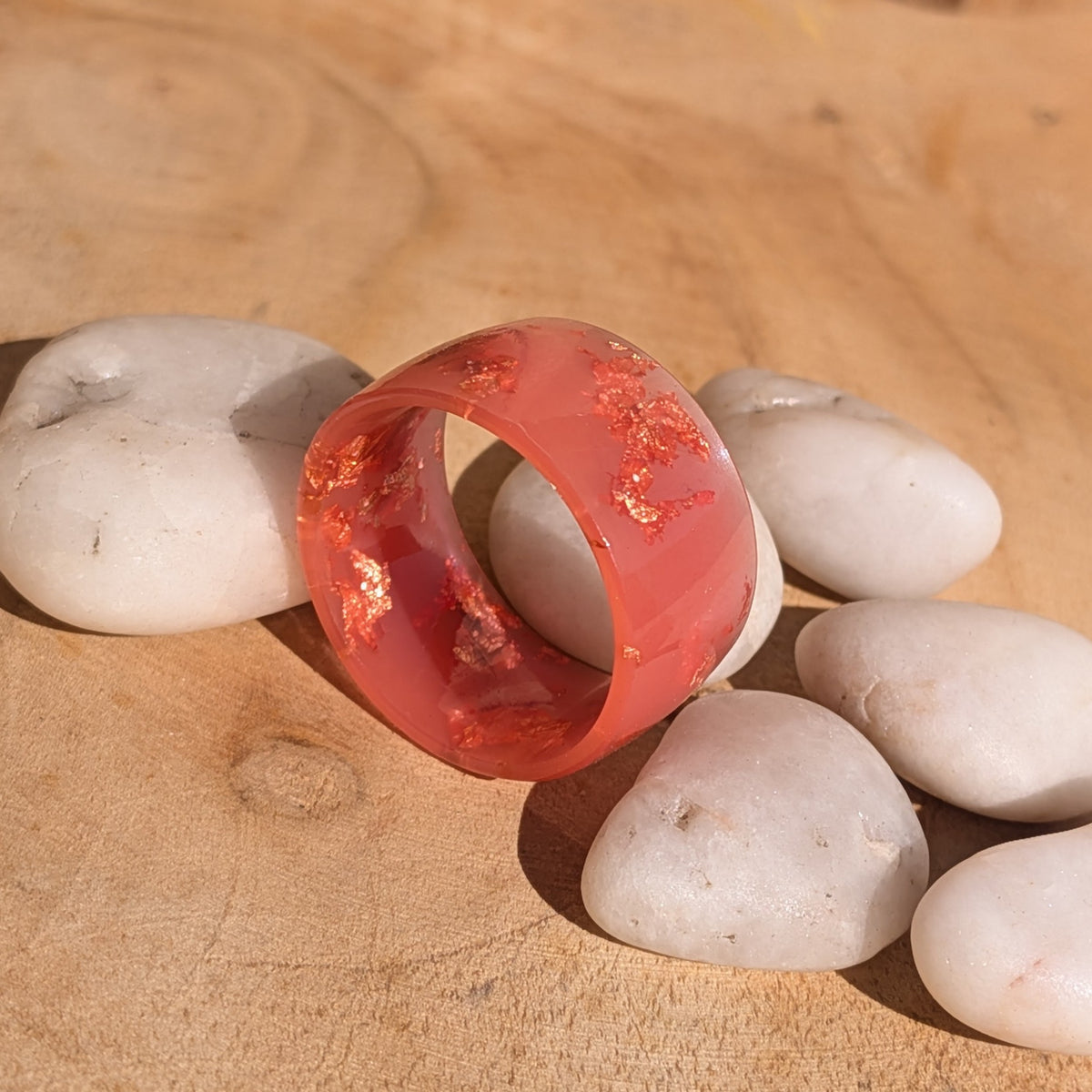 Milky pink resin ring standing upright among white stones, showing its circular opening and embedded copper flakes, EL-Creations
