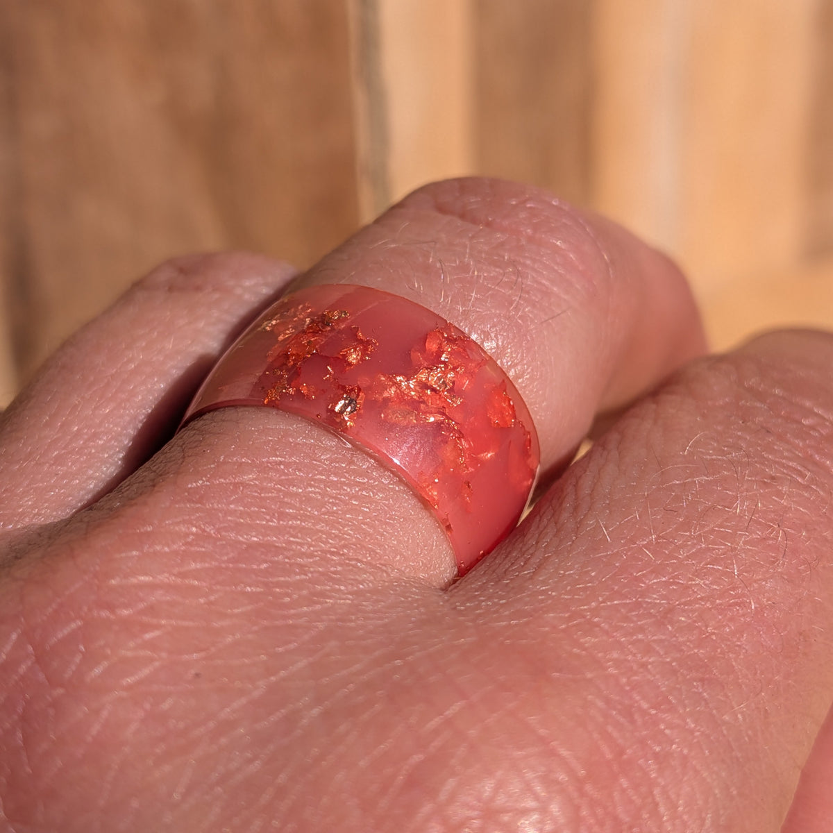 Macro close-up of a milky pink resin ring worn on a finger, showing irregular copper flakes within the band, EL-Creations
