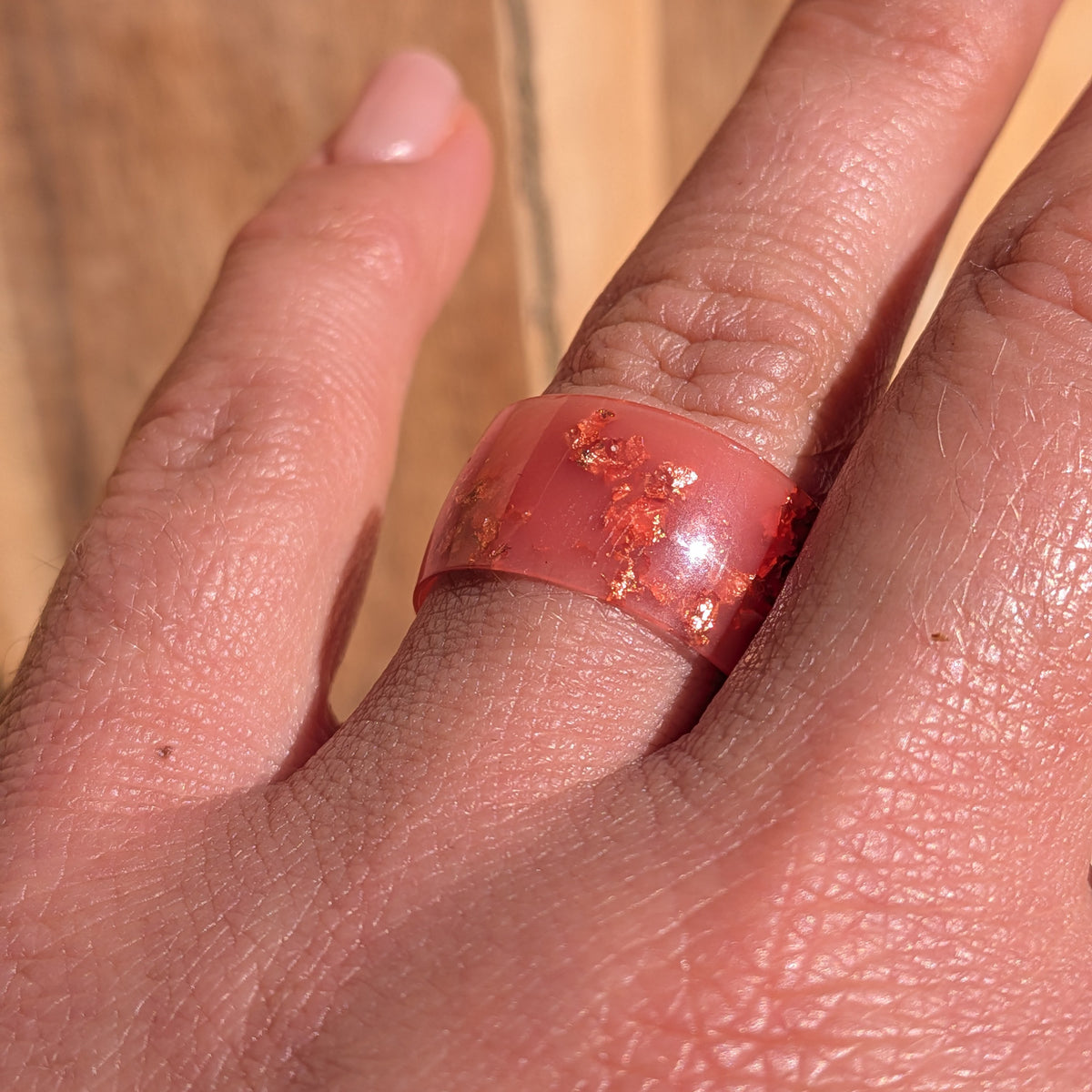 Angled close-up of a glossy milky pink copper flake resin ring worn on a hand in sunlight, EL-Creations