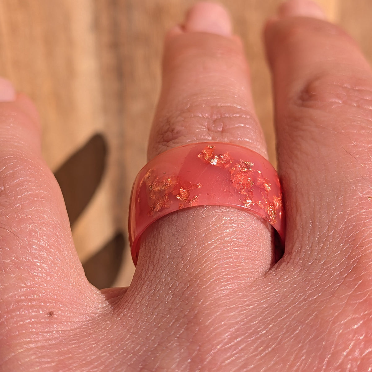 Front close-up of an 11 mm wide milky pink resin ring with shimmering copper flakes worn on a finger, EL-Creations