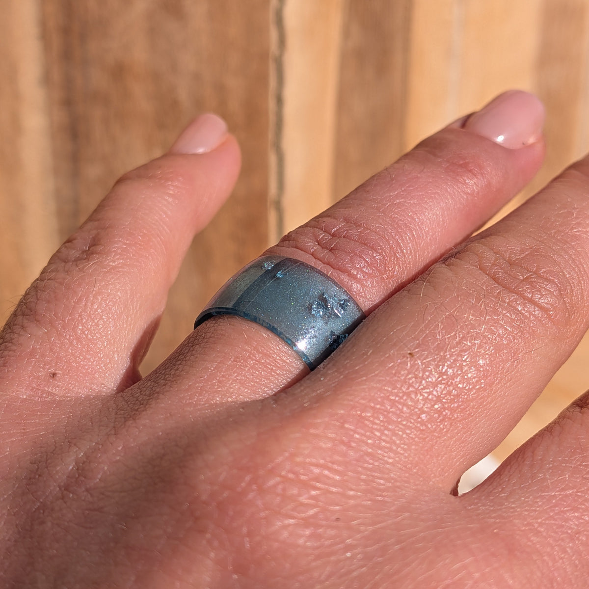 Blue resin statement ring with silver-coloured flakes worn on an outstretched hand in sunlight, EL-Creations