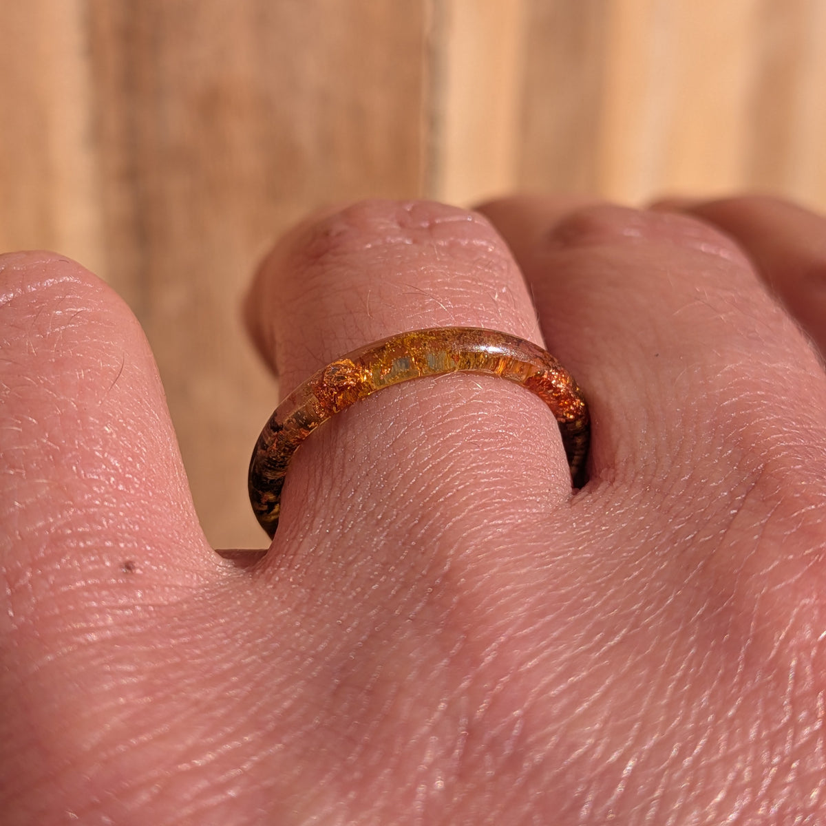 Low angled close-up of a fine moss resin ring with copper flakes worn on a finger in sunlight, EL-Creations