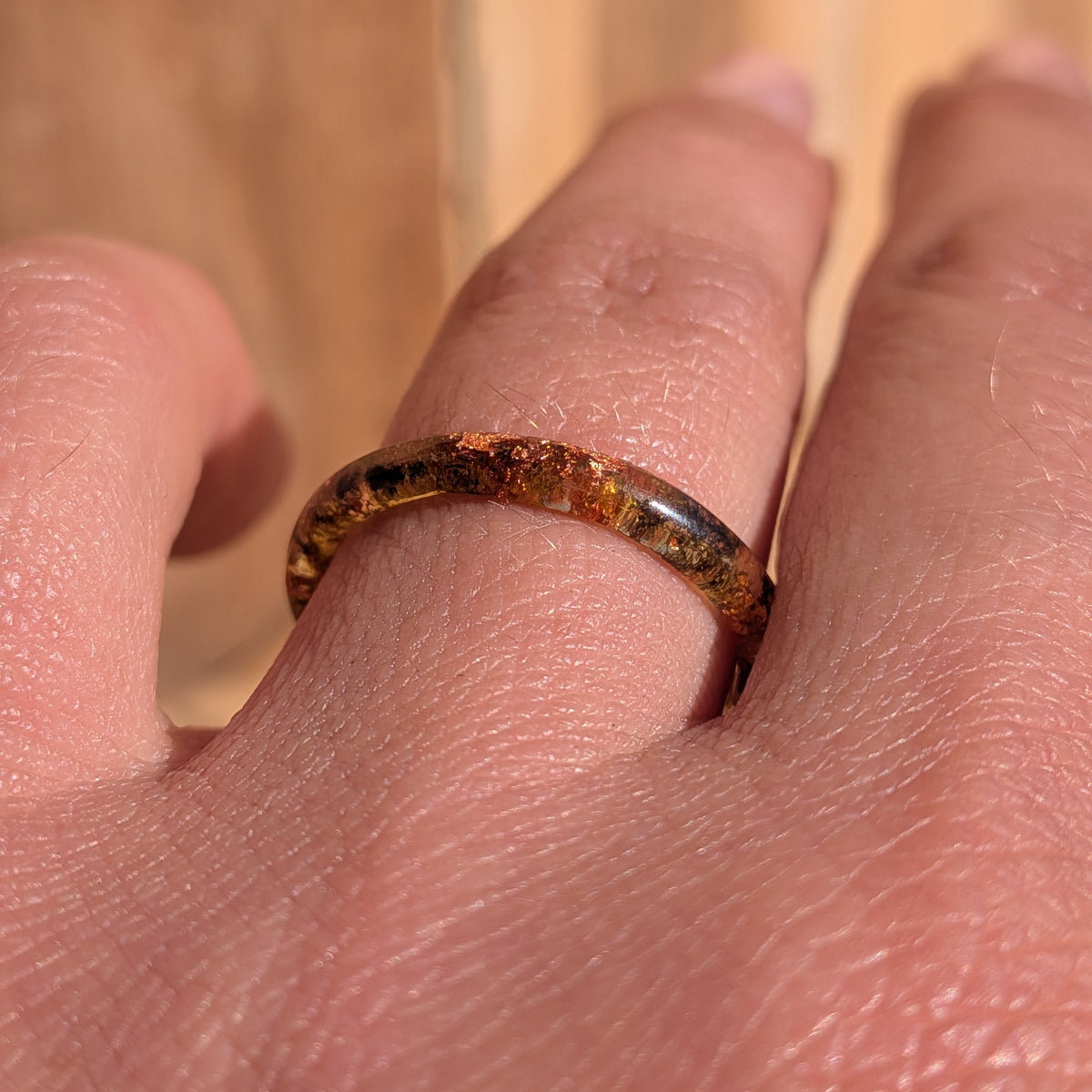 Front close-up of a thin resin ring with moss and copper flakes worn on a finger, EL-Creations