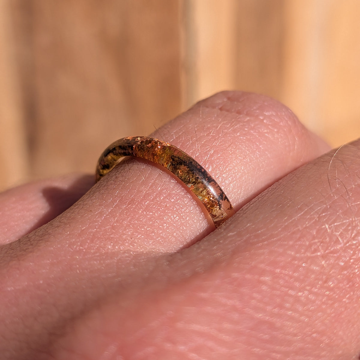 Side view of a delicate moss and copper flake resin ring worn on a finger, showing its slender rounded profile, EL-Creations