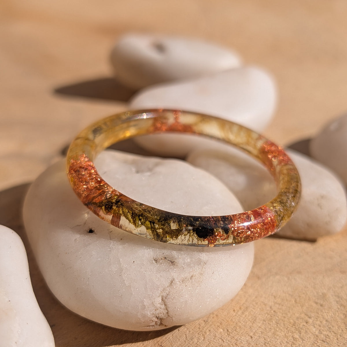 Close-up of a delicate resin ring with moss and copper flakes resting on a white pebble, showing botanical details inside the thin band, EL-Creations