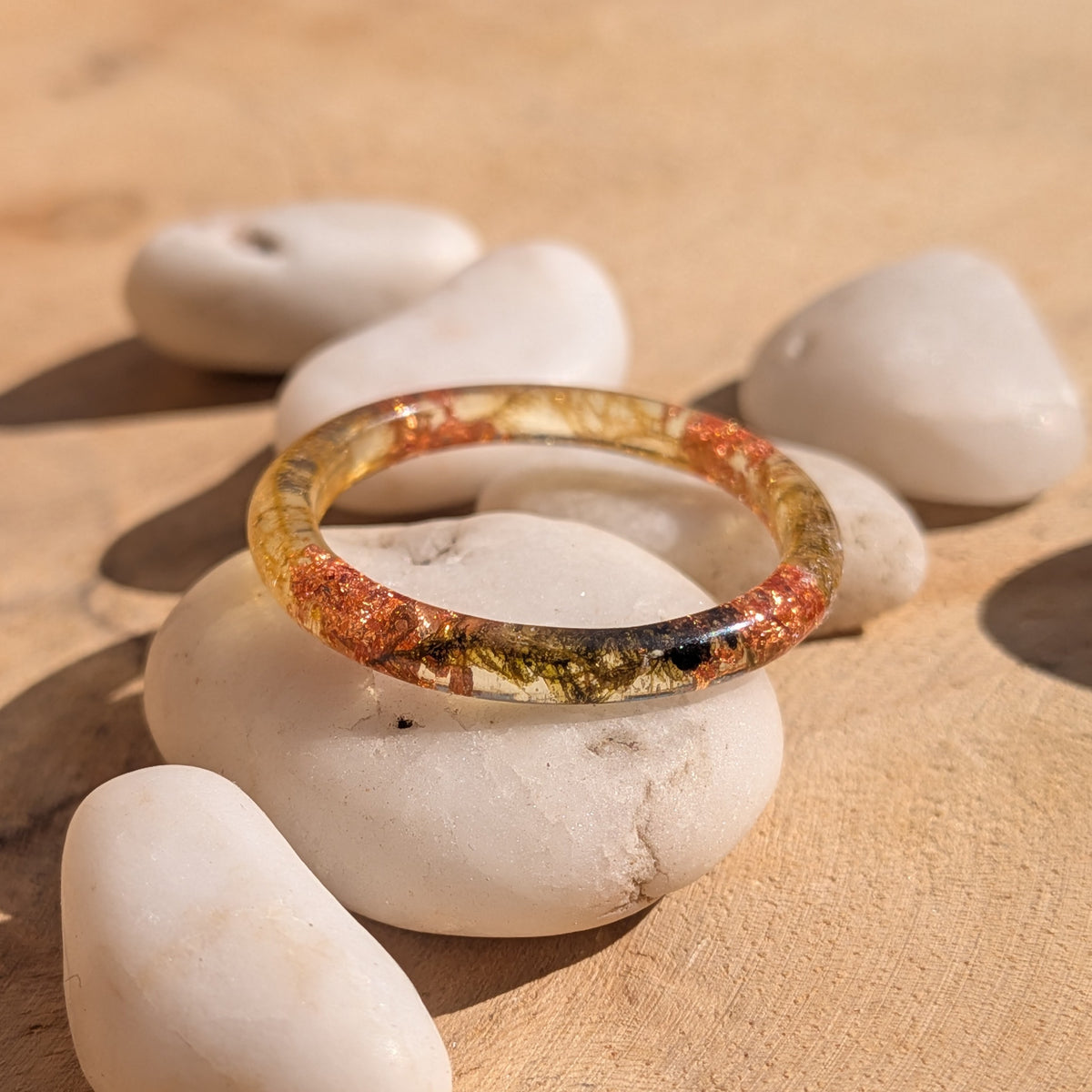 Fine resin ring with moss and copper flakes displayed on a white stone among pebbles on a wooden surface, EL-Creations