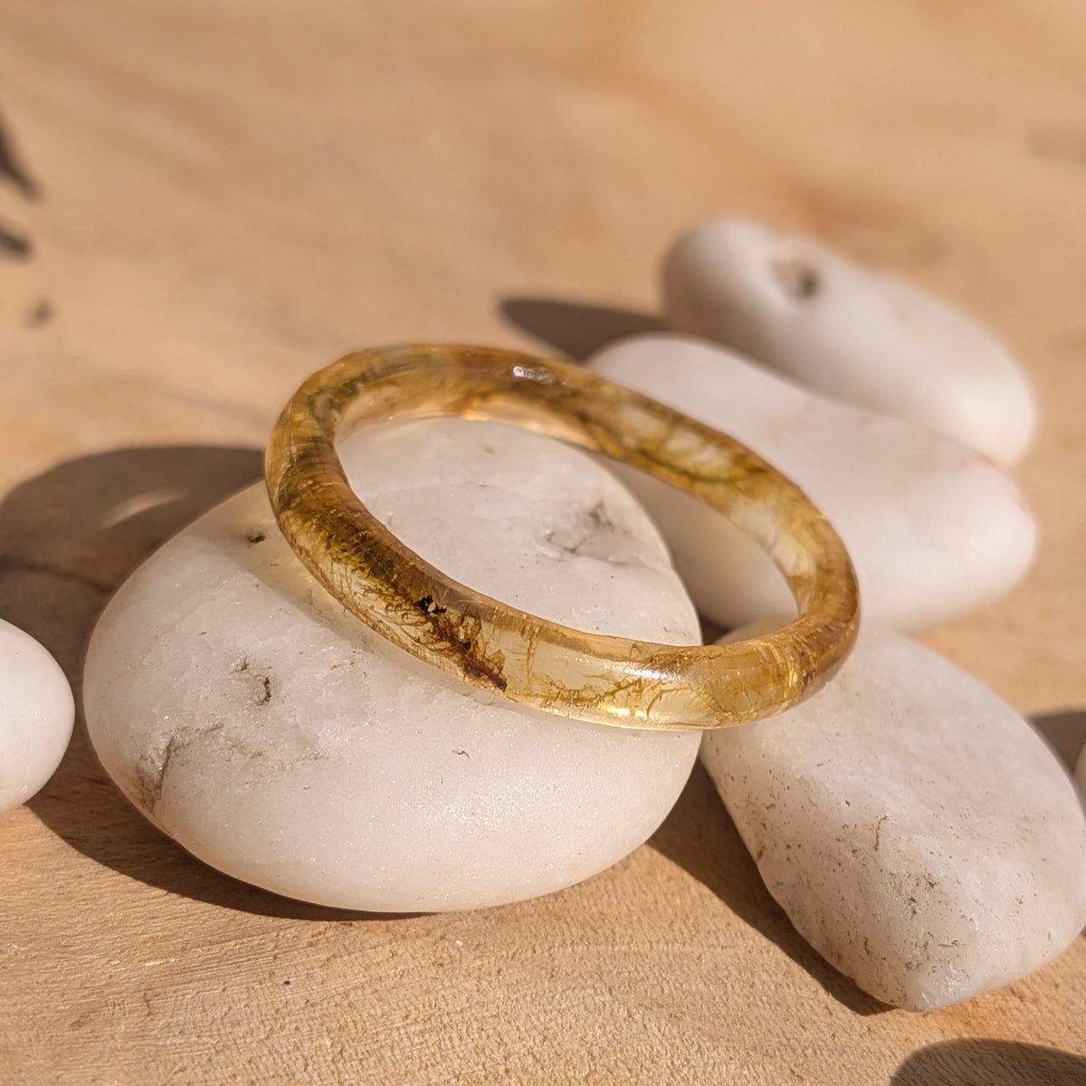 Angled view of a woodland moss resin ring resting across white stones, showing its fine rounded band, EL-Creations