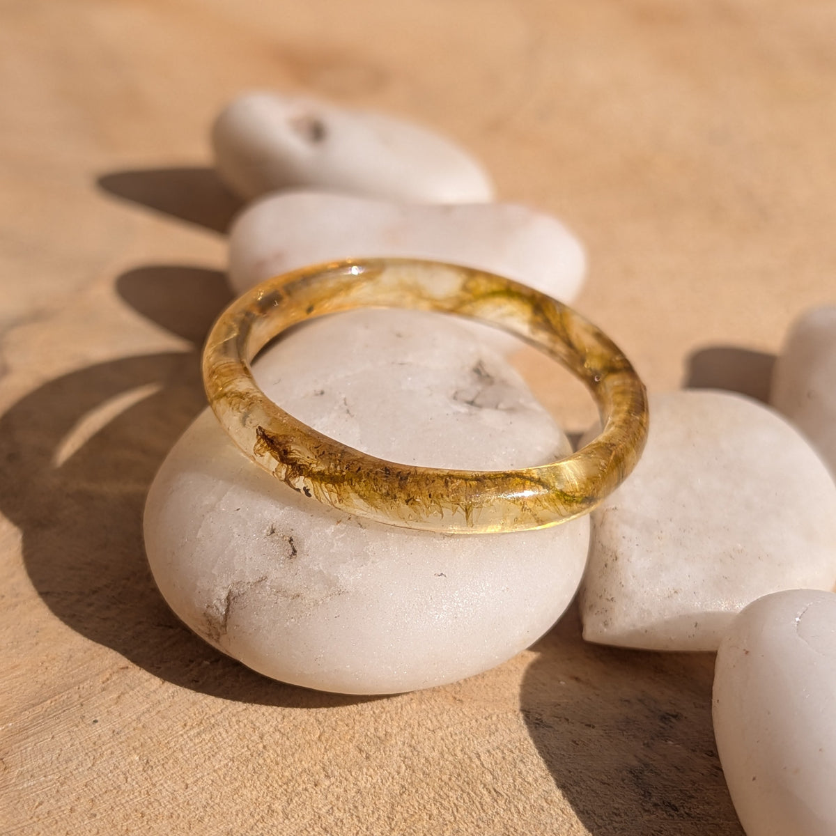 Delicate botanical resin ring containing moss, resting on white pebbles on a wooden surface, EL-Creations