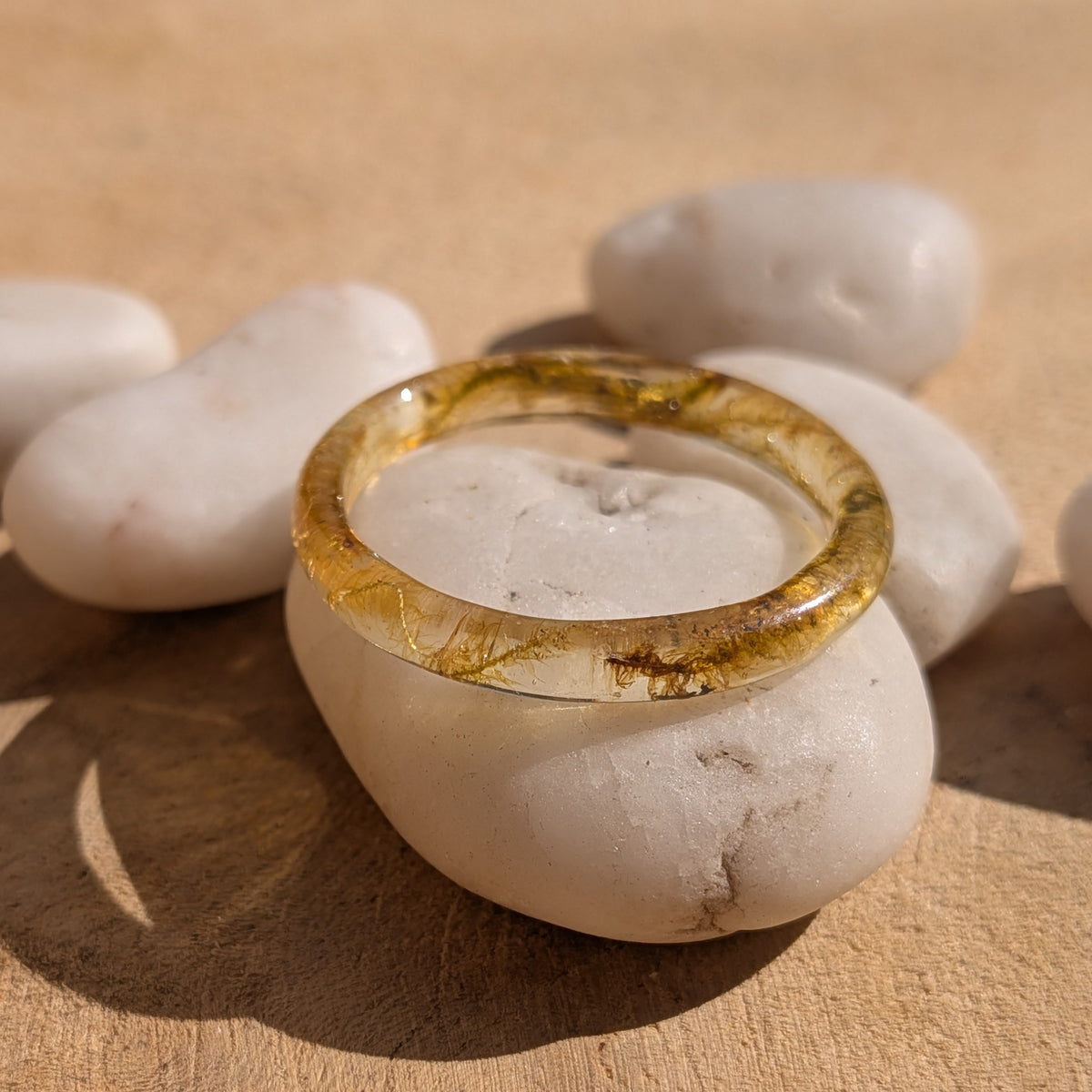 Thin moss resin ring displayed on a white stone in sunlight, with its circular opening visible, EL-Creations