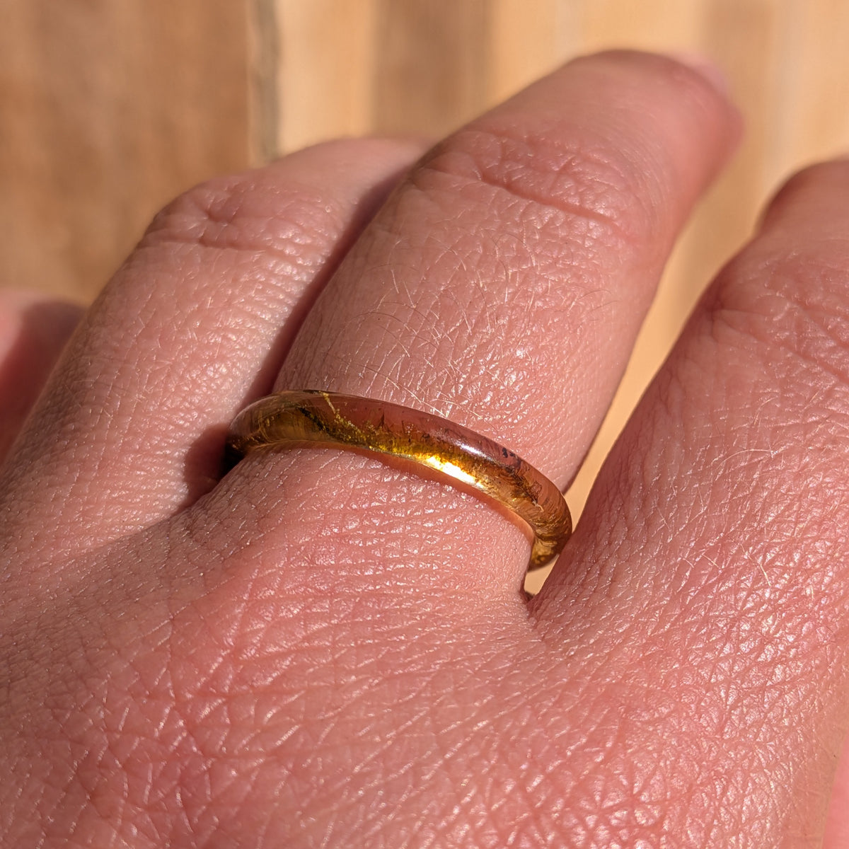 Close-up of a thin moss resin ring worn on a finger in sunlight, EL-Creations