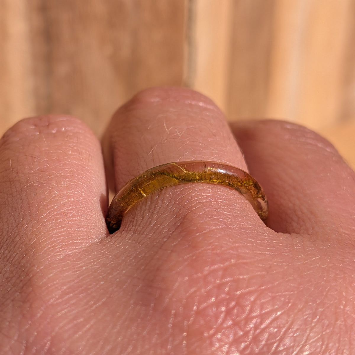 Front view of a slim woodland moss resin ring worn on a finger against a wooden background, EL-Creations