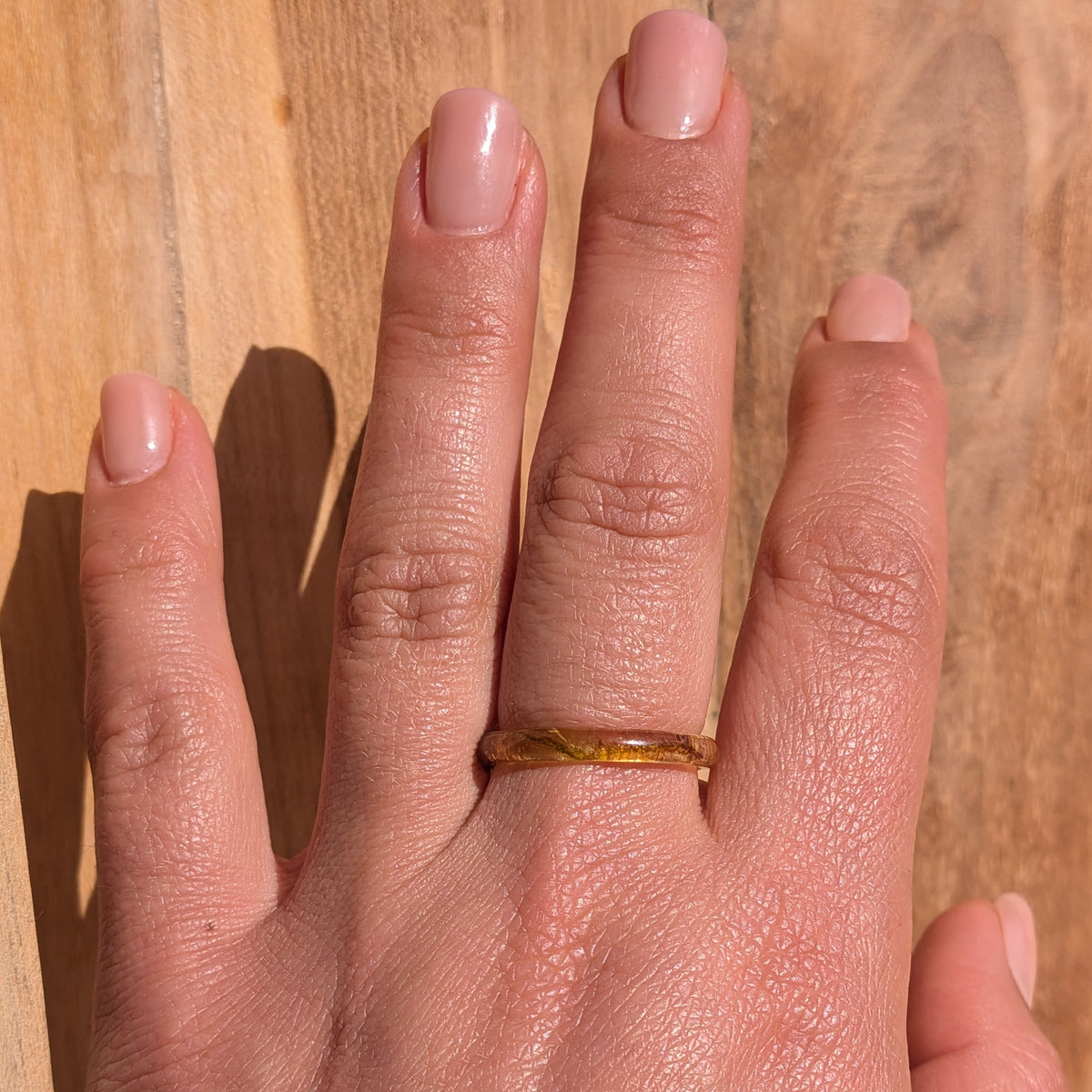Delicate moss resin ring worn on an outstretched hand in sunlight against a wooden background, EL-Creations