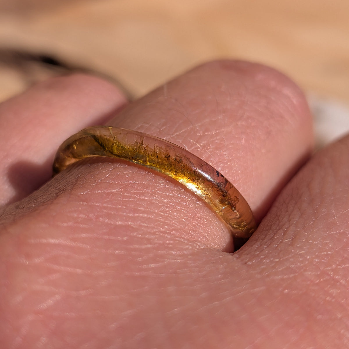 Macro close-up of moss preserved inside a glossy thin resin ring worn on a finger, EL-Creations