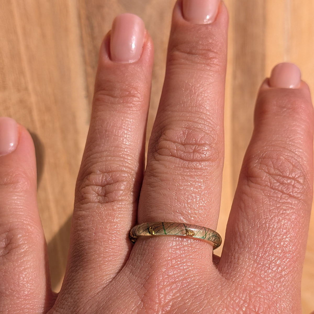 Delicate forest-green skeleton leaf resin ring with gold flakes worn on an outstretched hand against a wooden background, EL-Creations