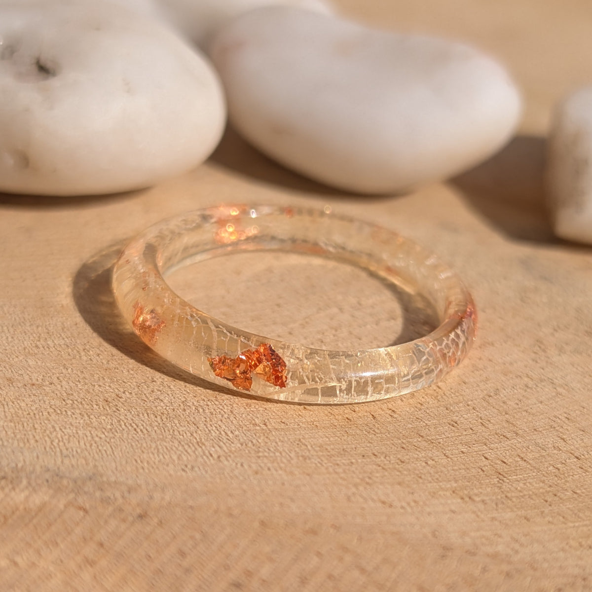 Slim white skeleton leaf resin ring with copper flakes lying on wood with white pebbles in the background, EL-Creations