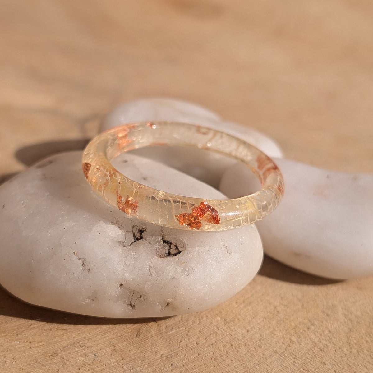 Delicate resin ring with white skeleton leaf veins and copper flakes resting at an angle on a white pebble, EL-Creations