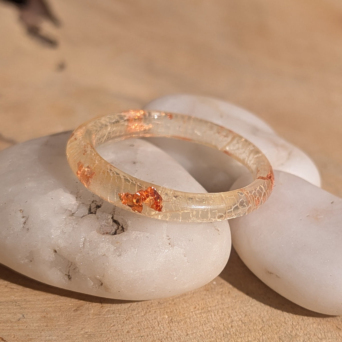 Close-up of a white skeleton leaf resin ring on white stones, showing copper flakes beneath its glossy surface, EL-Creations