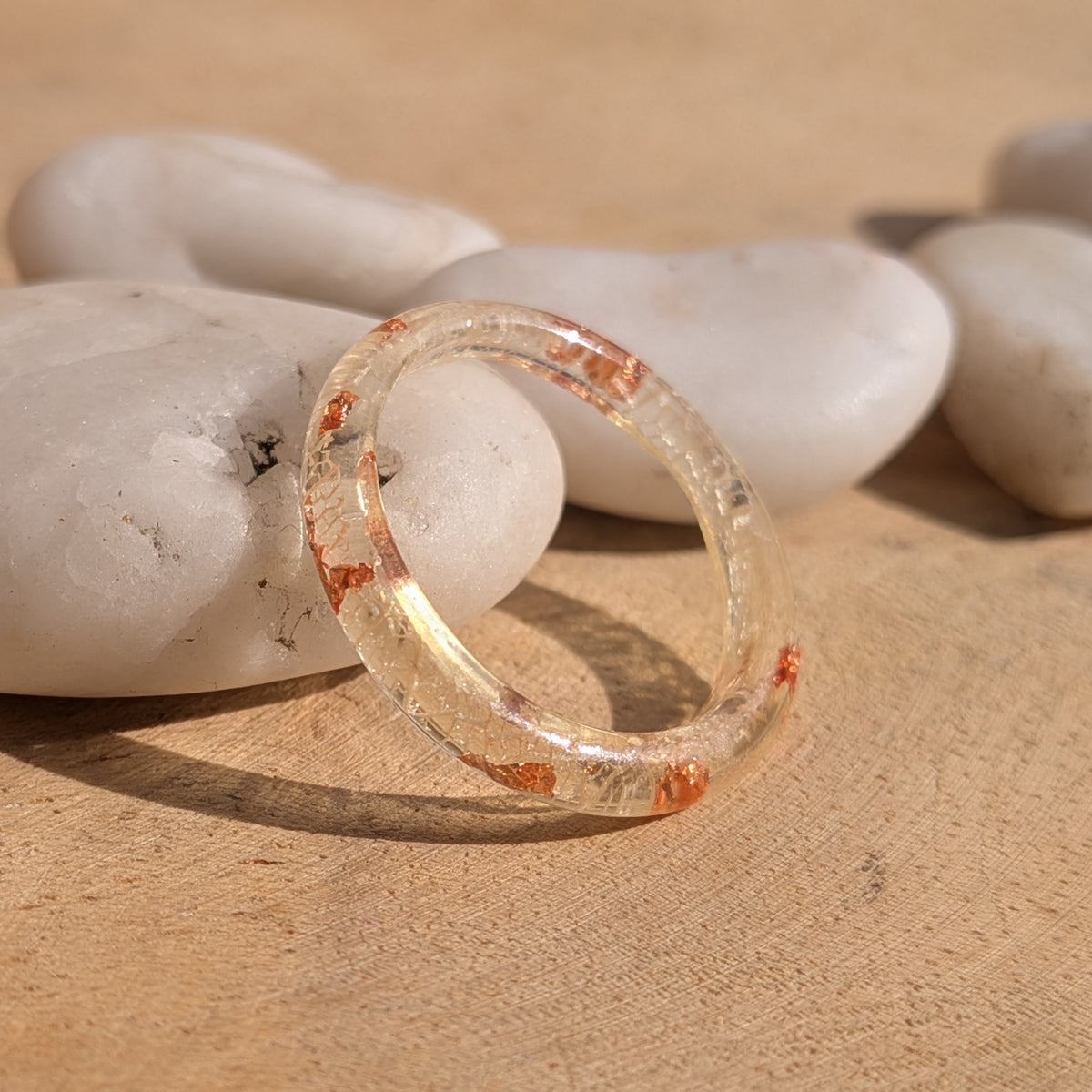 Thin resin ring with white skeleton leaf veins and copper flakes standing upright against a white pebble, EL-Creations