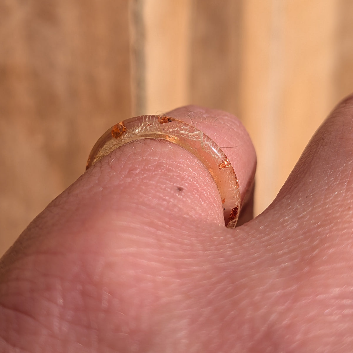 Angled macro view of a white skeleton leaf resin ring with copper flakes worn on a finger in sunlight, EL-Creations