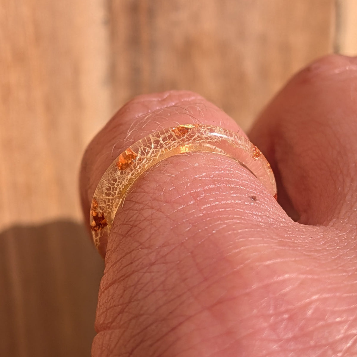 Front macro close-up of white leaf veins and copper flakes inside a delicate resin ring worn on a finger, EL-Creations