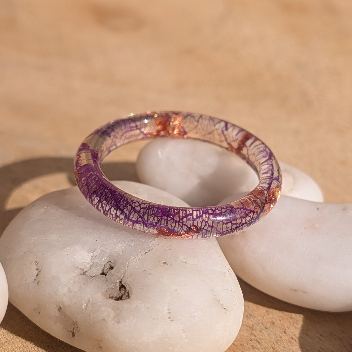 Close-up of a purple skeleton leaf resin ring on white pebbles, showing its intricate leaf pattern and glossy band, EL-Creations