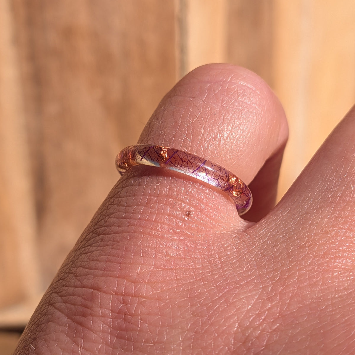 Angled close-up of a delicate purple skeleton leaf resin ring with copper flakes worn on a finger in sunlight, EL-Creations