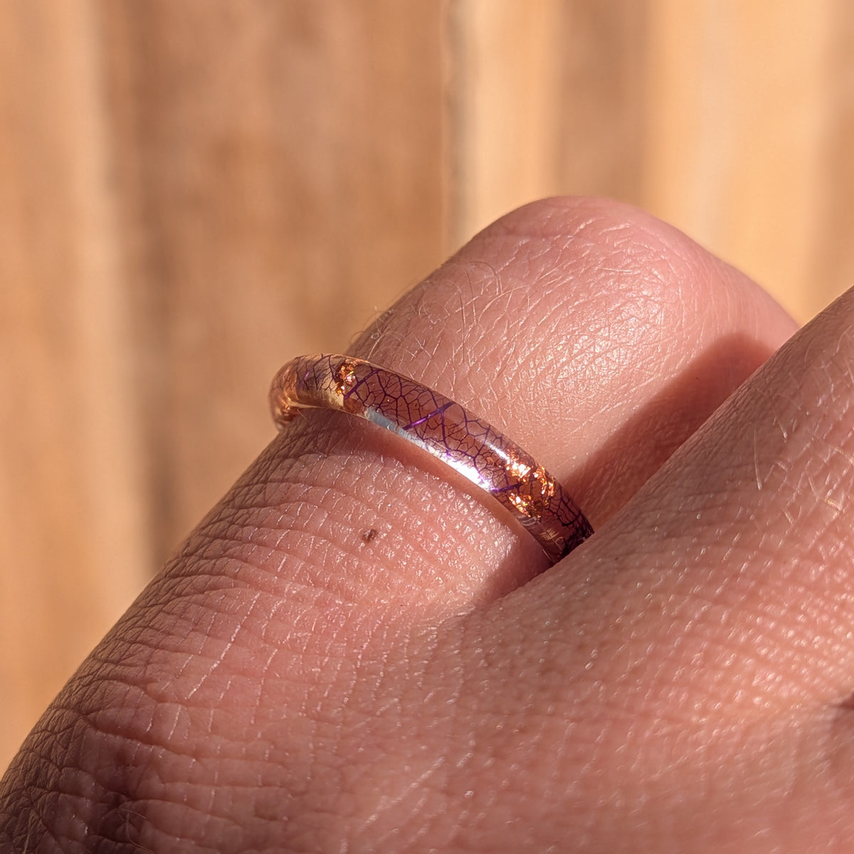 Side macro view of a purple skeleton leaf resin ring with copper flakes worn on a gently bent finger, EL-Creations