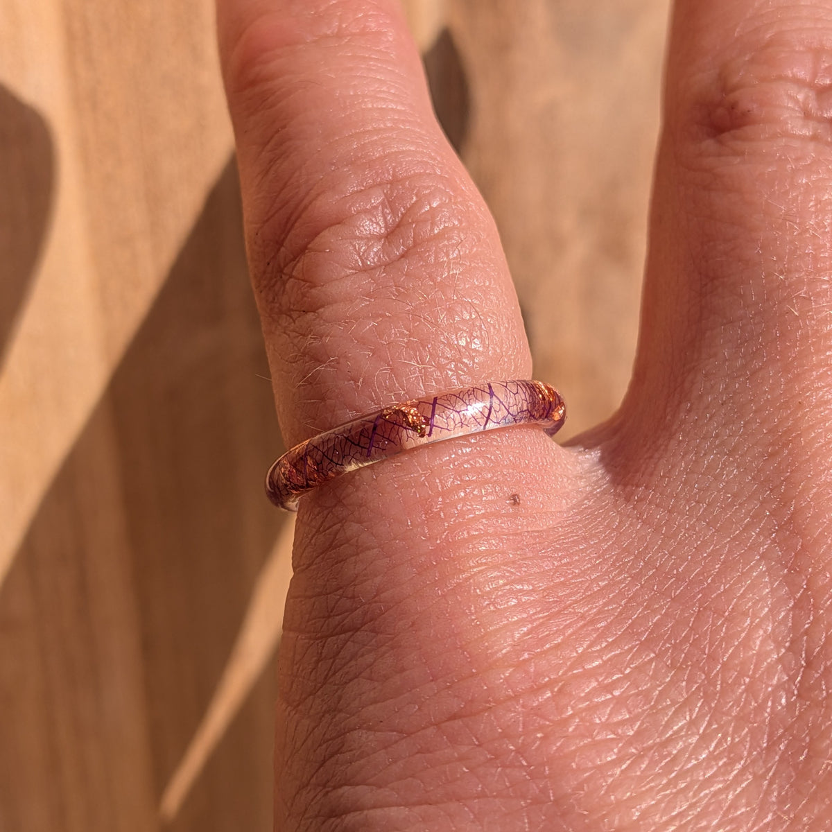 Delicate purple skeleton leaf resin ring with copper flakes worn on an extended finger in sunlight, EL-Creations