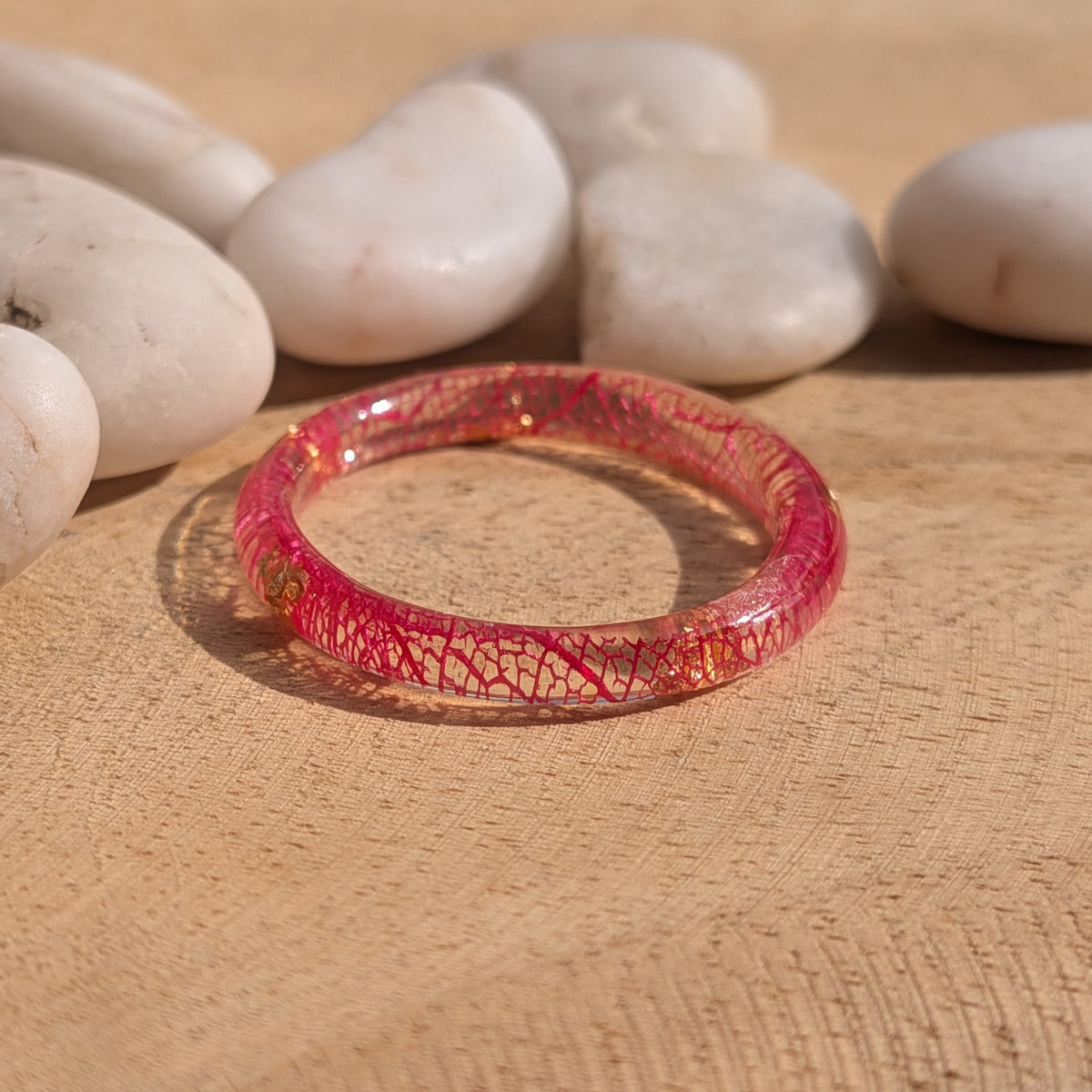 Angled view of a red skeleton leaf resin ring with copper flakes lying on a sunlit wooden surface, EL-Creations